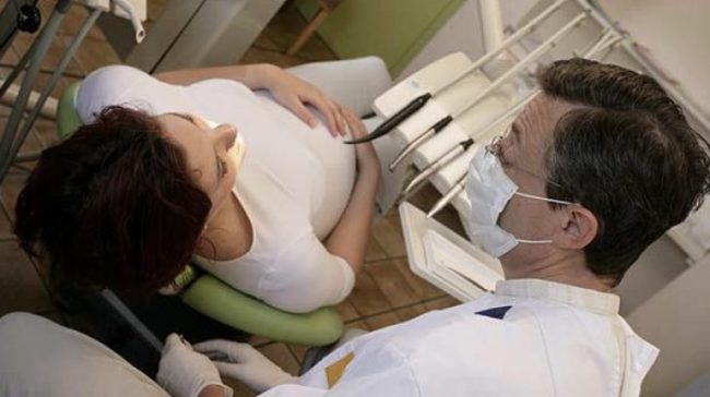 Беременная женщина удаляет зуб у стоматолога