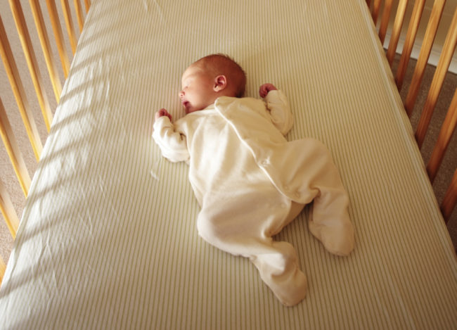 Новорождённый спит в детской кроватке