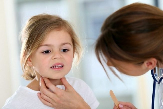 Взрослая женщина проверяет горло маленькой девочки со светлыми волосами и каримиглазами 