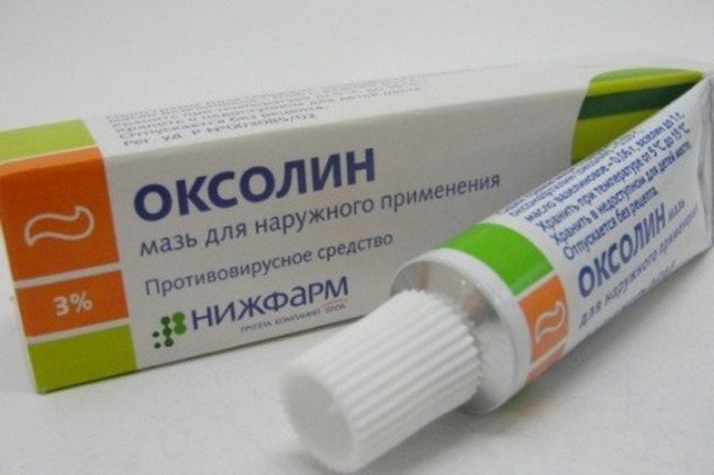 На белом фоне бело-зелёная упаковка с лекарственной мазью "Оксолин"