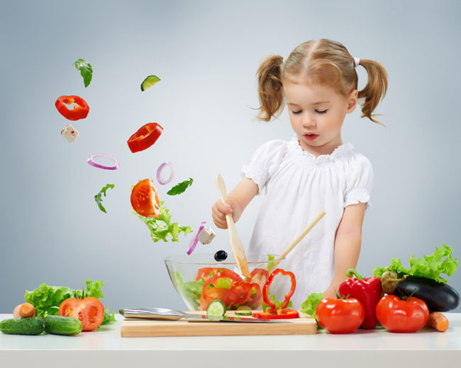 Девочка у стола делает салат из свежих овощей, перемешивает содержимое салатника