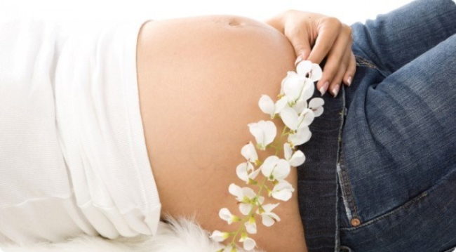 Живот беременной женщины и белый цветок в руке