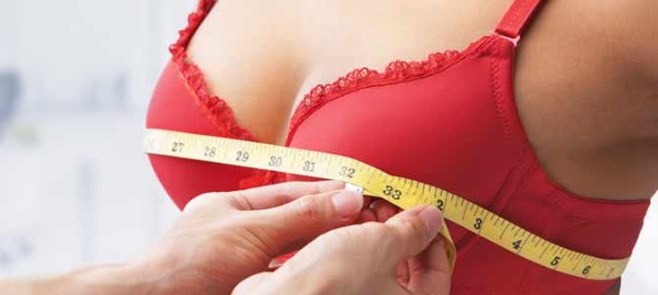 Девушка в красном бюстгальтере измеряют объём груди