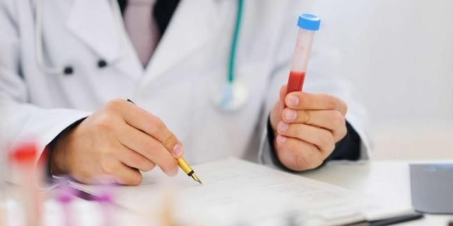 Анализ крови в руке врача пишущего ручкой на бумаге