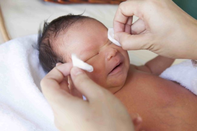 Новорождённой девочке протирают глазки ватным мокрым диском