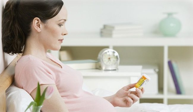 Первый триместр беременности у женщины и таблетки в руке