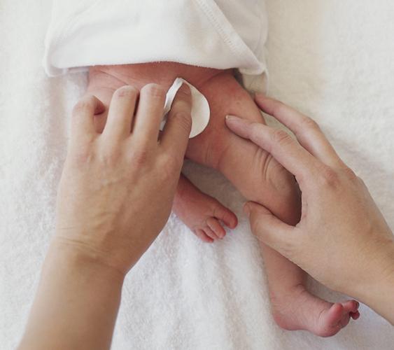 Обработка белым ватным диском половых губ у новорожденной девочки в белой кофточке