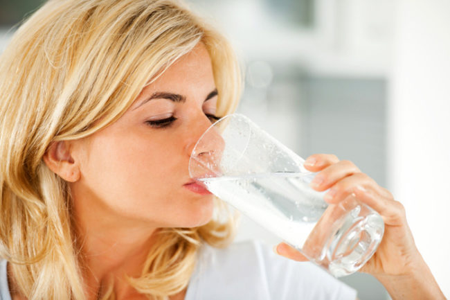 Женщина со светлыми волосами пьющая воду из прозрачного стакана