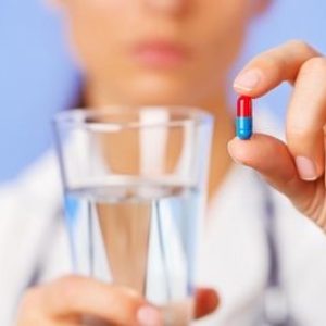 В руках врача стакан с водой и сине-красная капсула лекарства