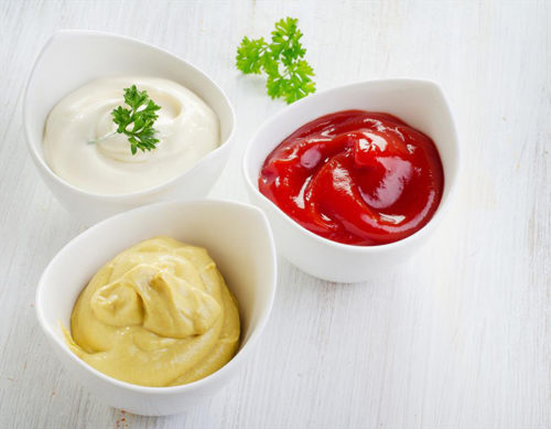 Майонезный соус в белой пиалке с зелёной петрушкой и красный кетчуп в белой пиалке