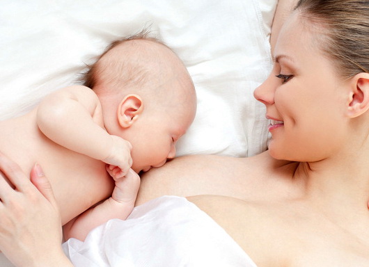 Новорождённый ребёнок лежа сосет грудь своей мамы