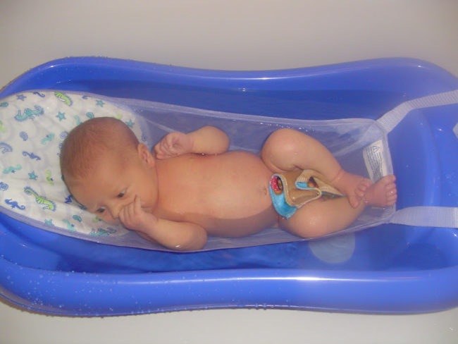 Новорождённый купается в ванночке