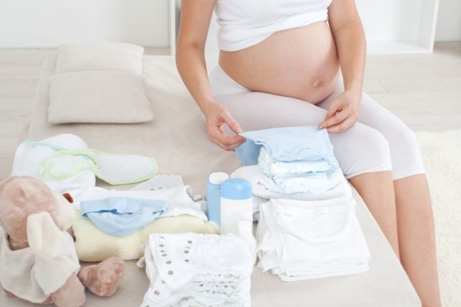 Беременная на позднем сроке собирает вещи для новорождённого
