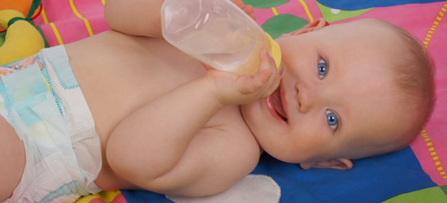 Маленький, голенький ребенок с бутылочкой лежит на цветной пеленке