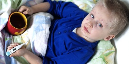Мальчик в синией пижаме лежит в кровати с чашкой и градусником с признаками краснухи