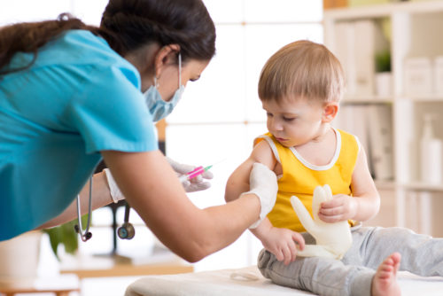 Ребенку делает прививку медсестра в синем халате