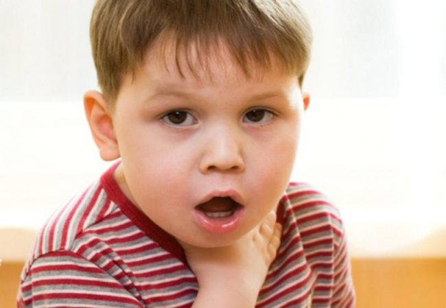 Маленький мальчик в полосатой футболке с карими глазами рукой держится за горло