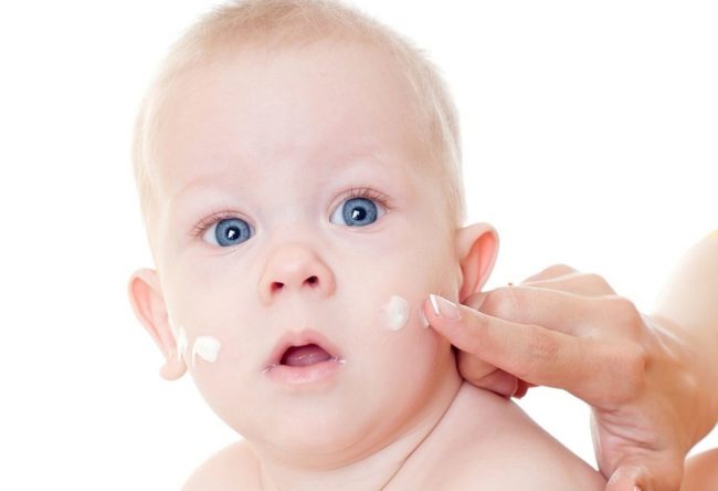 Нанесение крема для лица на щёки голубоглазого ребёнка