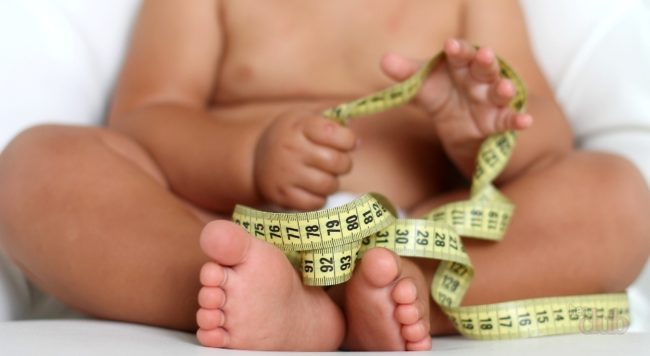 Ребёнок страдающий ожирением держит в руках измеритель метр