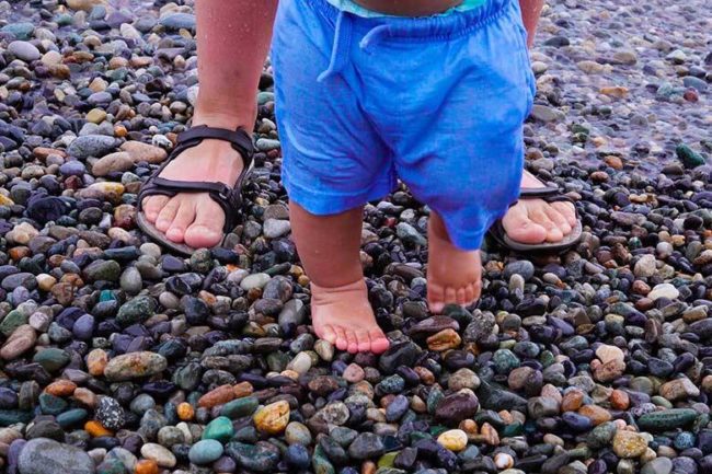 Маленький ребёнок ходит по камням на море под присмотром родителей