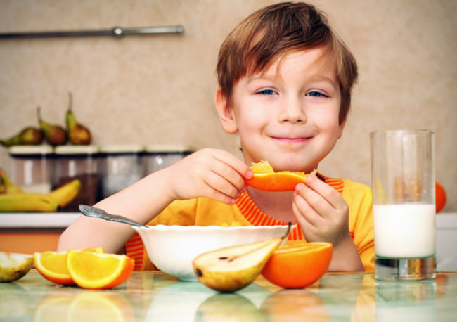 Мальчик сидит за столом и ест апельсин