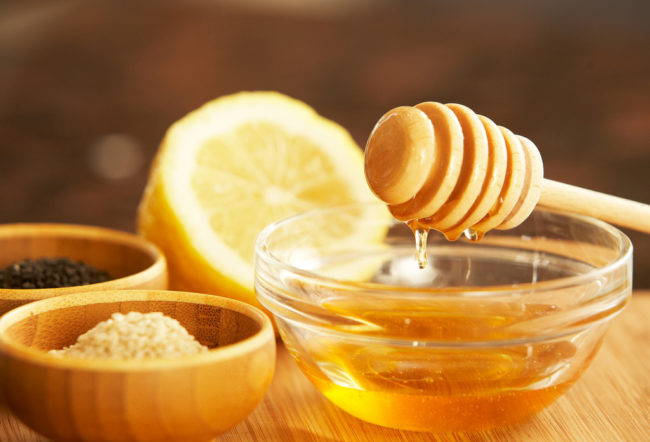На столе стоят миски с медом и приправами, сзади лежит половинка лимона