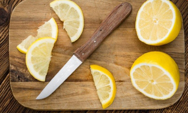 Свежепорезанные дольки лимона на разделочной доске и нож